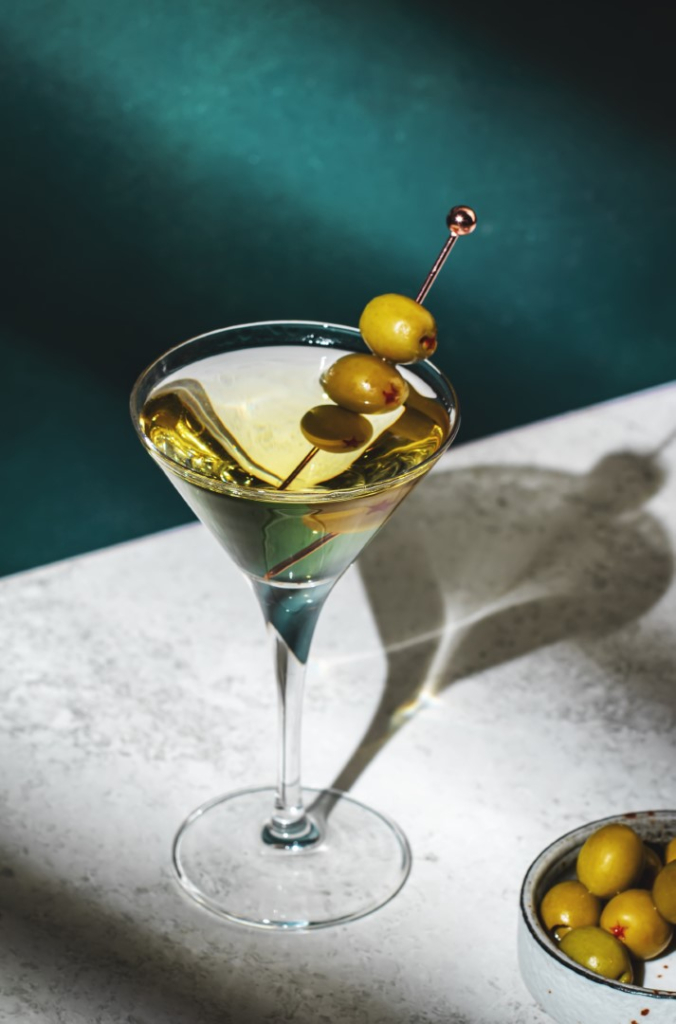 Vodka martini, klasični alkoholni koktajl z vodko in vermutom, okras iz zelenih oliv, temno ozadje, svetla trda svetloba in vzorec senc