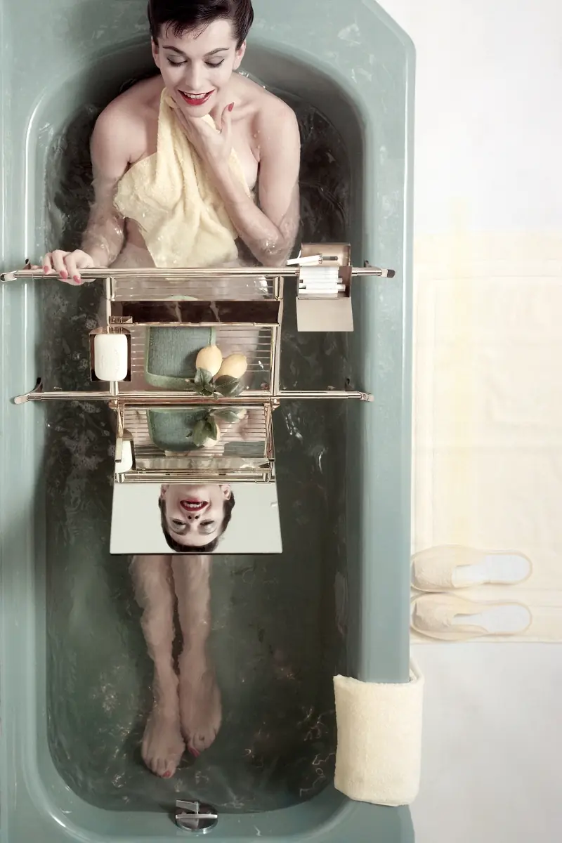 Model in bathtub shot from above with her face reflected in mirror on tub rack