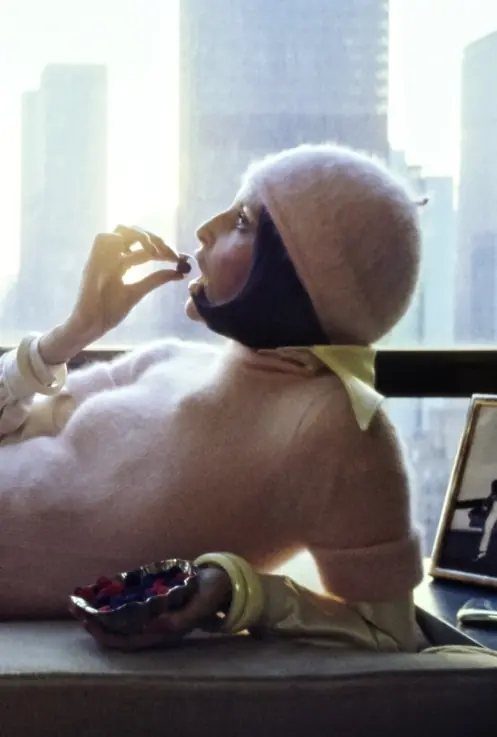 Model reclining by a window with sunrise and a skyline behind her. She wears a pink knit bodysuit from Chadbourn, made of angora, wool, and nylon. It is styled with a yellow shirt from Blousecraft by Maxime de la Falaise, made of crêpe-backed satin of acetate and nylon. Accessories include a beret by Irving Paul for Capadors, Donald Stannard bangle on left wrist, Alexis Kirk cuff on right. Vogue July 01, 1972 Fashion Feature
