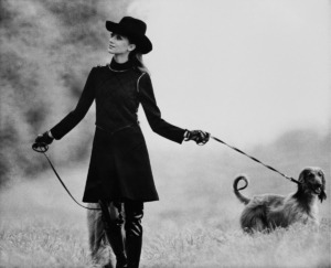 Actress and model Marisa Berenson walking in a field with two Afghan hounds and wearing black wool jersey gilet with buckles at shoulders and sides, trimmed with contrasting piping, and diamond-patterned bodice by Mic Mac; long-sleeved black jersey turtleneck dress; black riding derby by Gelot for Mic Mac; thigh-high patent leather boots by Carel; Hair by Carita *** Local Caption *** Marisa Berenson; Vogue August 01, 1968 Portrait