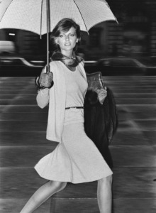 Model Cheryl Tiegs, walking under an umbrella by Mespo, holding a fur coat, and wearing a long angora and wool cardigan, matching sleeveless pullover, and skirt by Habitat, with belt and bag by Manon , Cheryl Tiegs; Vogue September 01, 1973 Fashion