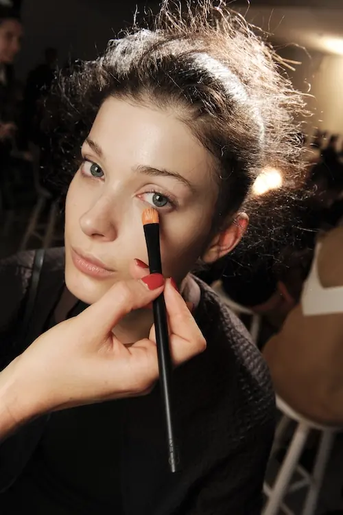 Phillip Lim Spring 2015 RTW vizažist nanosi korektor za podočnjake modelu u backstageu