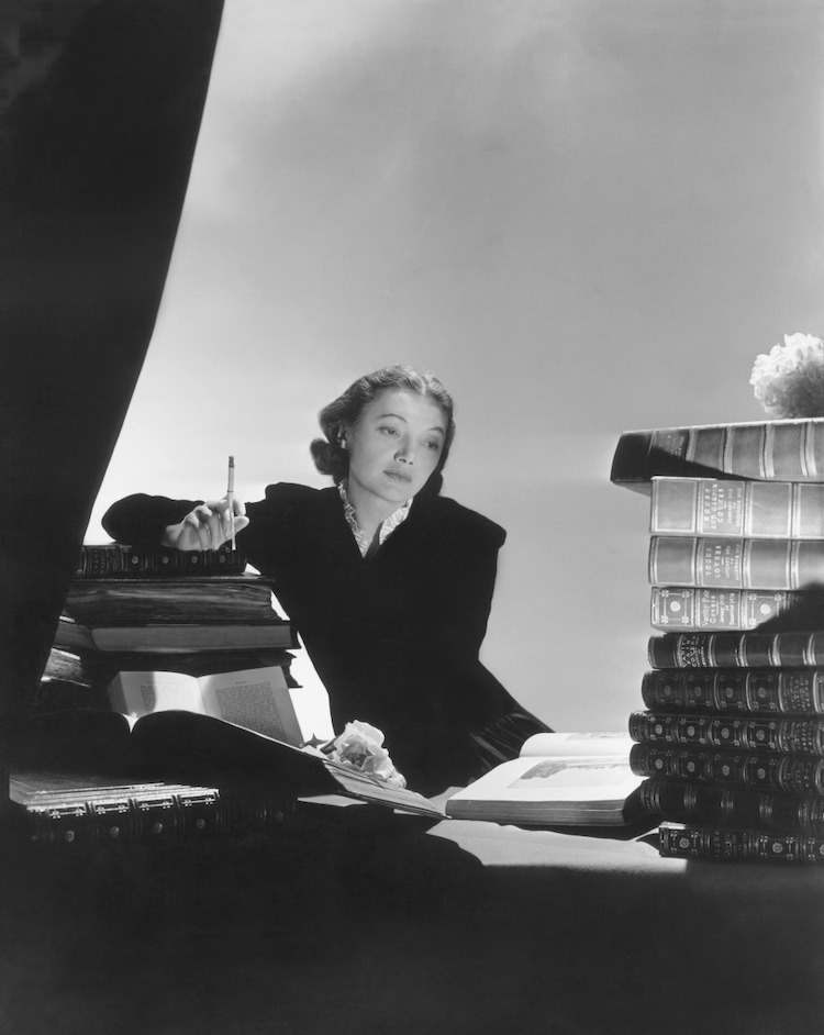 Actress Katharine Cornell wearing a black jacket, white ruffles showing at the neckline, surrounded by books *** Local Caption *** Katharine Cornell; Vogue February 01, 1938 Portrait