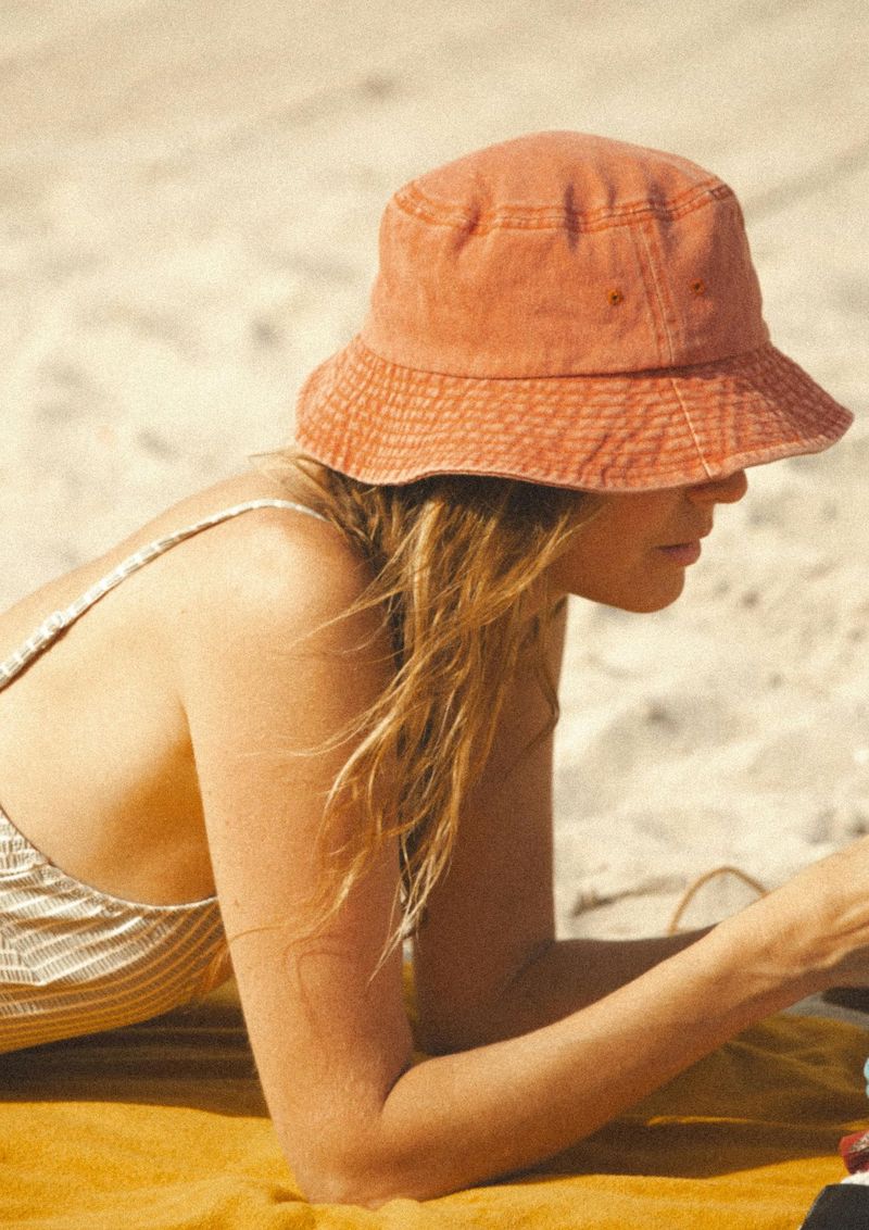 žena leži na plaži i sunča se s narančastom kapom na glavi