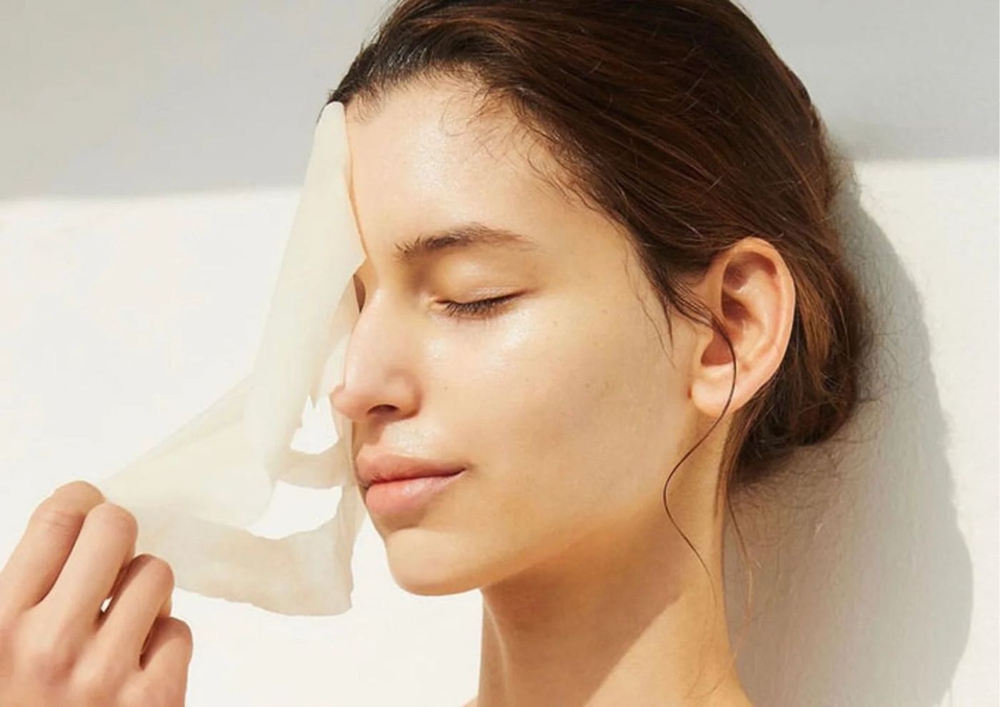 žena skida sheet masku s lica dok se sunča