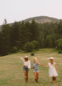 tri djevojke se smiju i trče po livadi među planinama