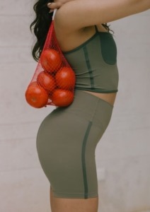 model u maslinastom kompletu za vježbanje drži vrećicu s rajčicama