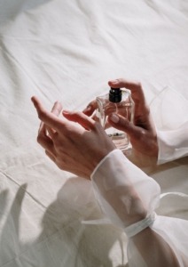 žena s bijelom bluzom nanosi parfem na ruku