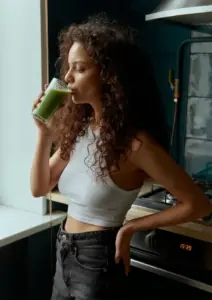 žena s kovrčavom kosom pije zeleni detox sok