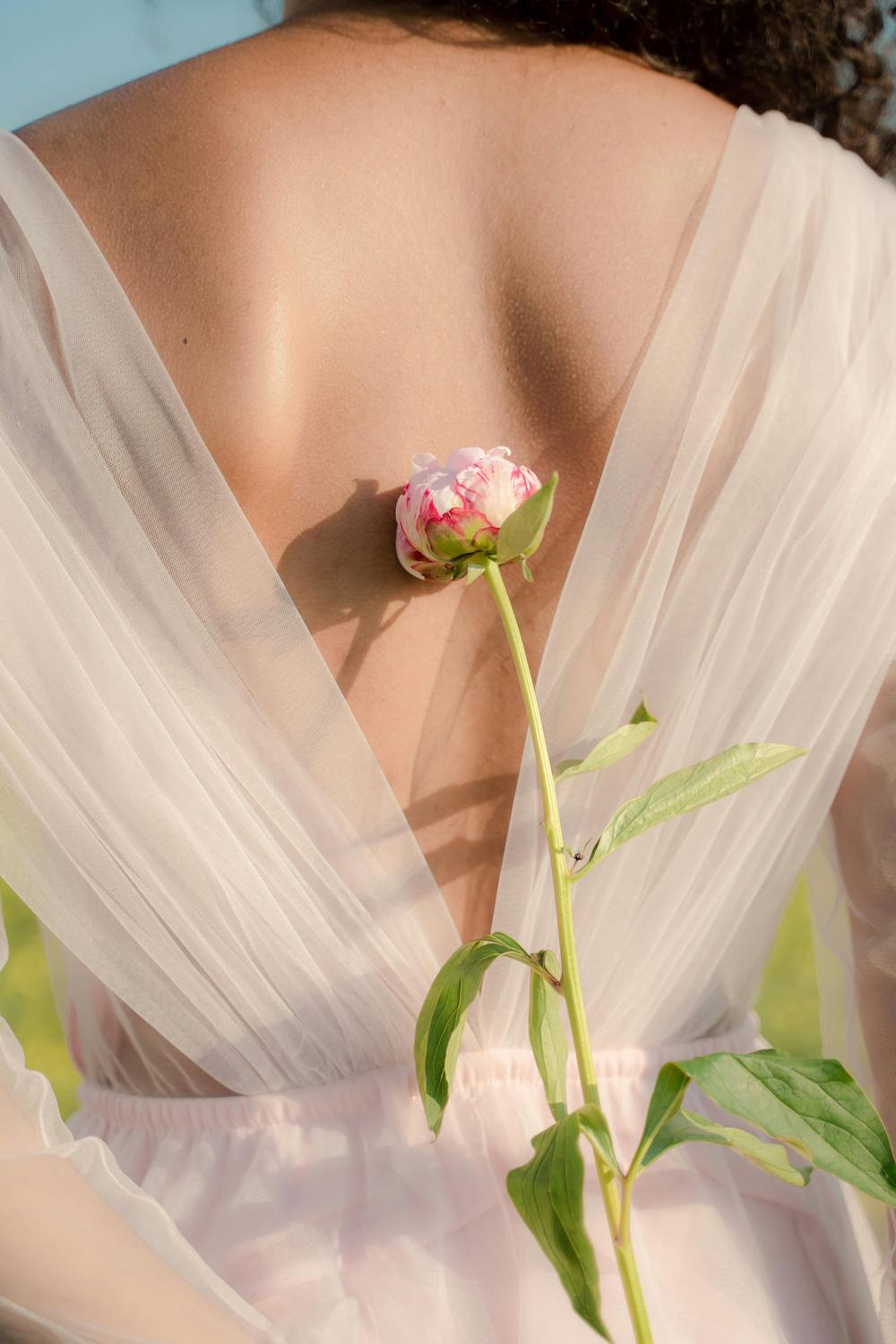 žena u bijeloj haljini bez leđa drži rozu ružu